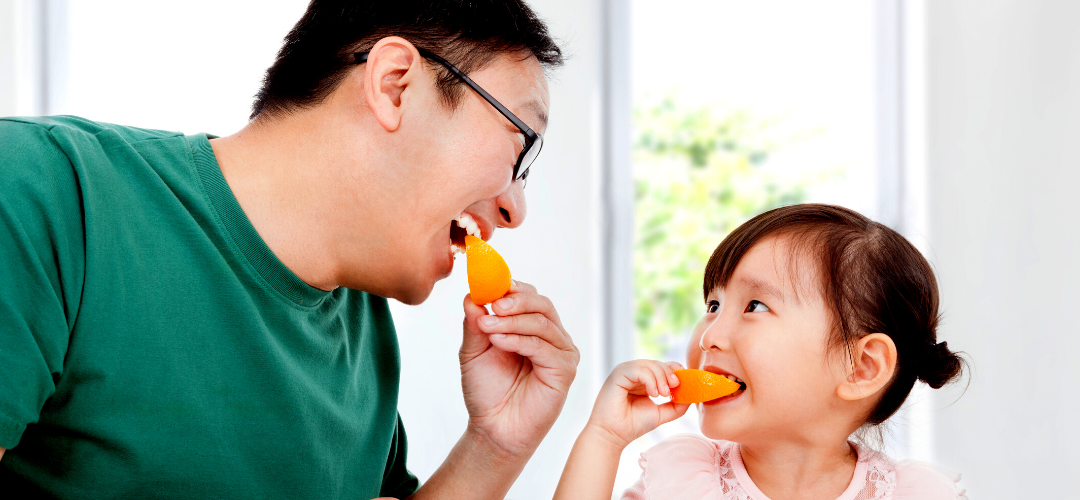 Adult male and female child eating oranges which contains essential vitamins for healthy teeth and gums.