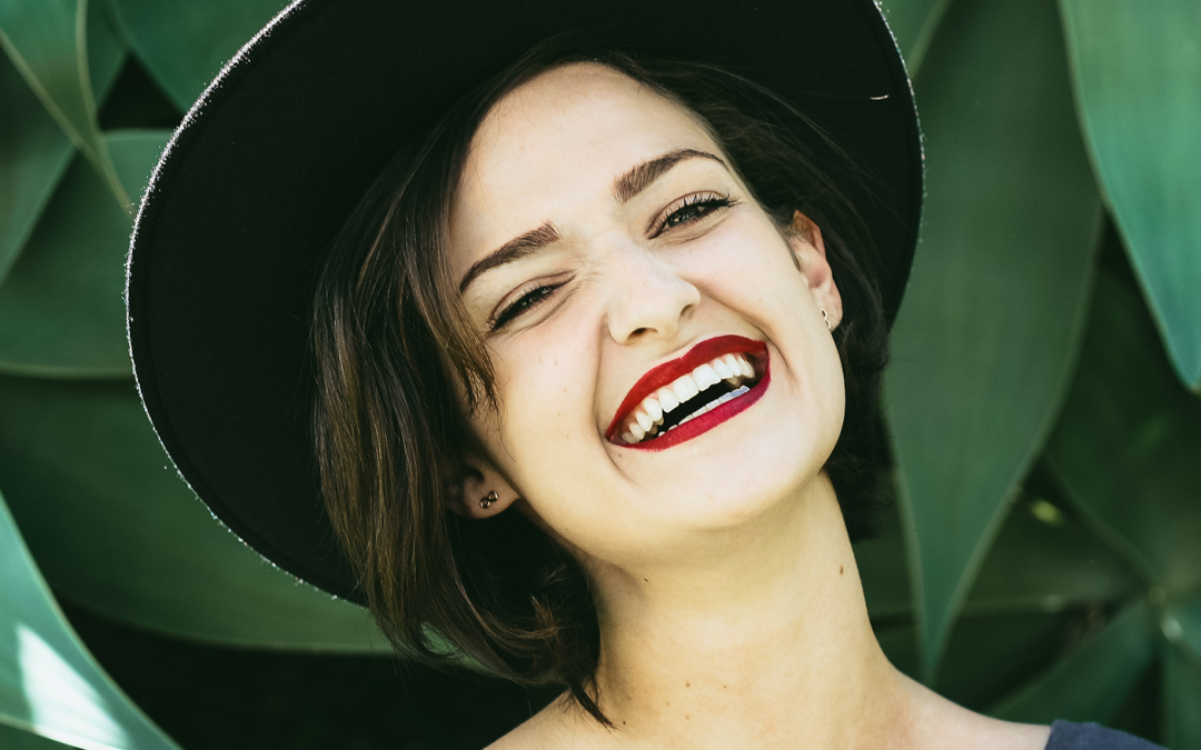 Woman wearing a hat and red lipstick smiles broadly