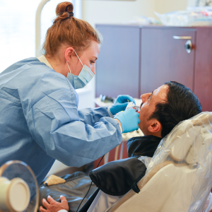 A resident cleans a patient's teeth